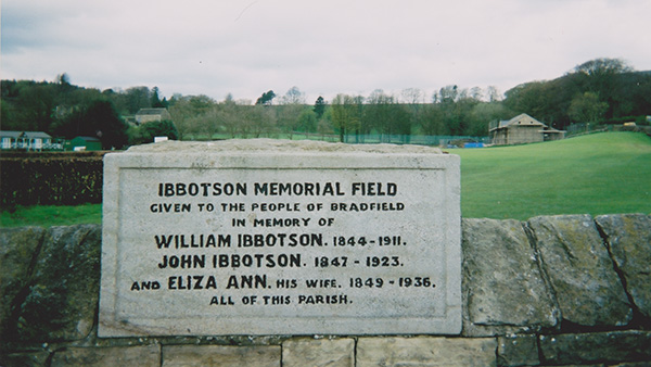 An engraved block of stone in the top of a wall with a green field behind it.
